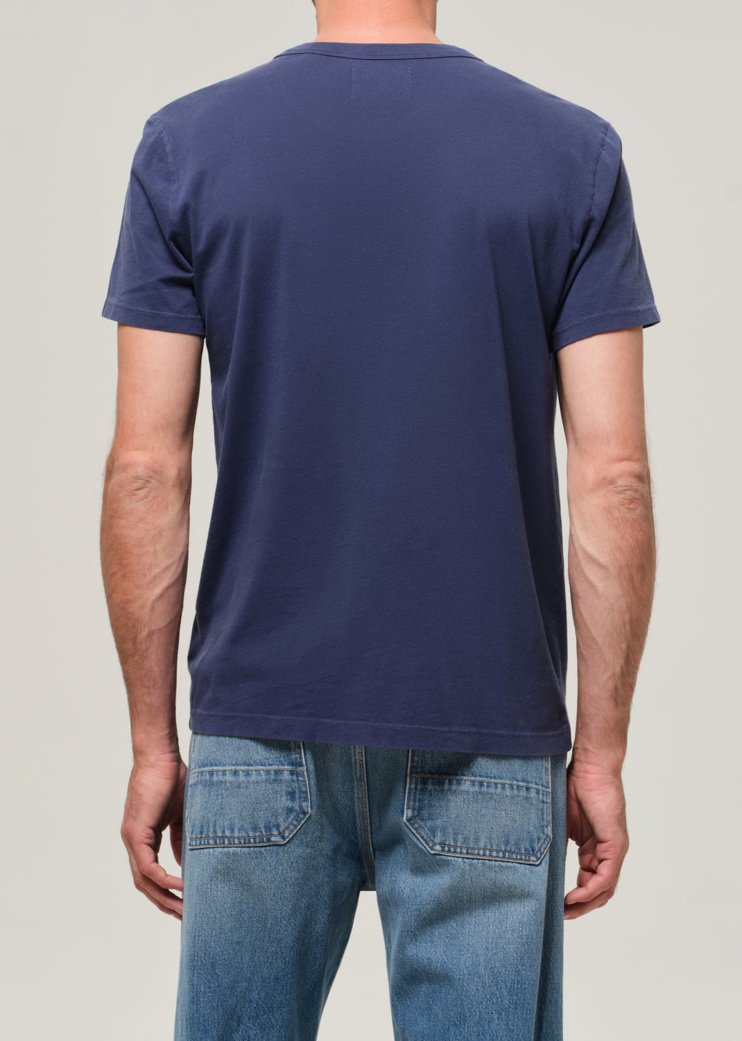 Person wearing a navy blue t-shirt and light blue jeans on a plain background