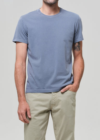 Man wearing a blue t-shirt and beige pants against a gray background