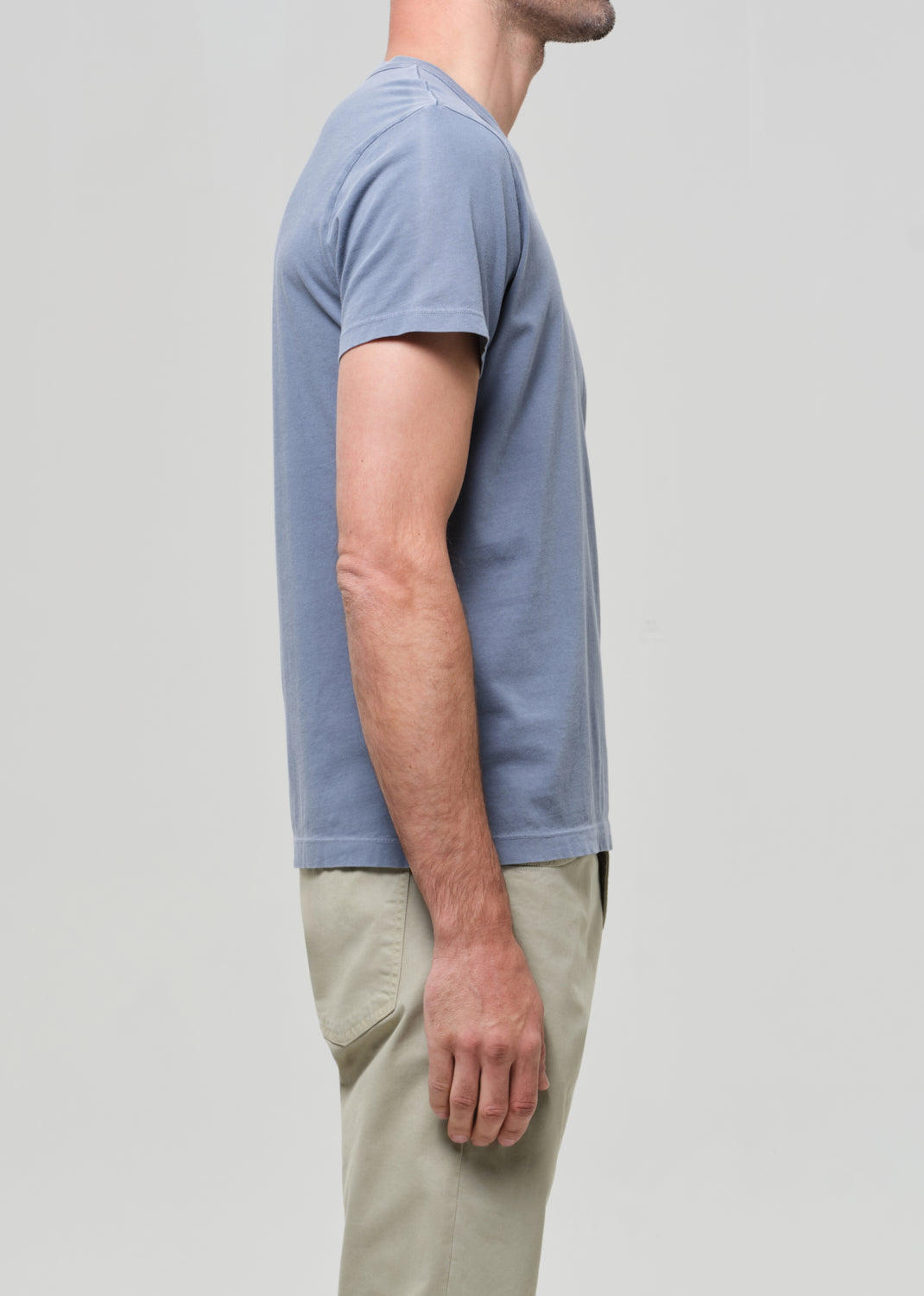 Person wearing a light blue t-shirt and beige pants on a plain background