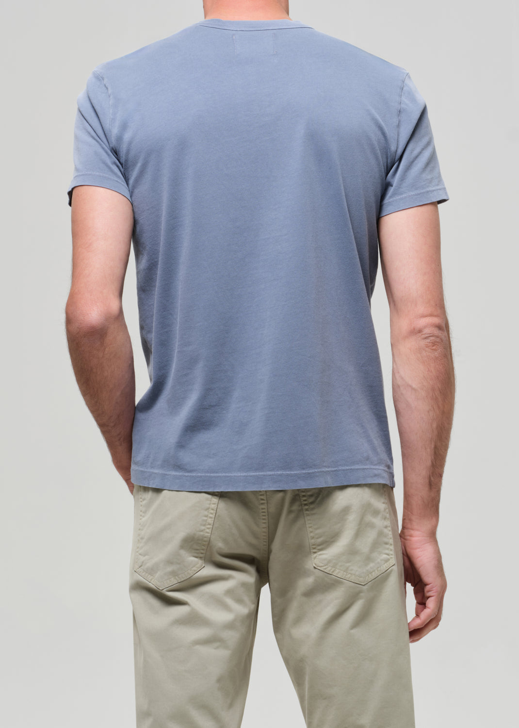Person wearing a light blue t-shirt and beige pants on a plain background