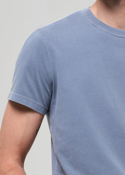 Close-up of a person wearing a plain blue t-shirt against a light gray background