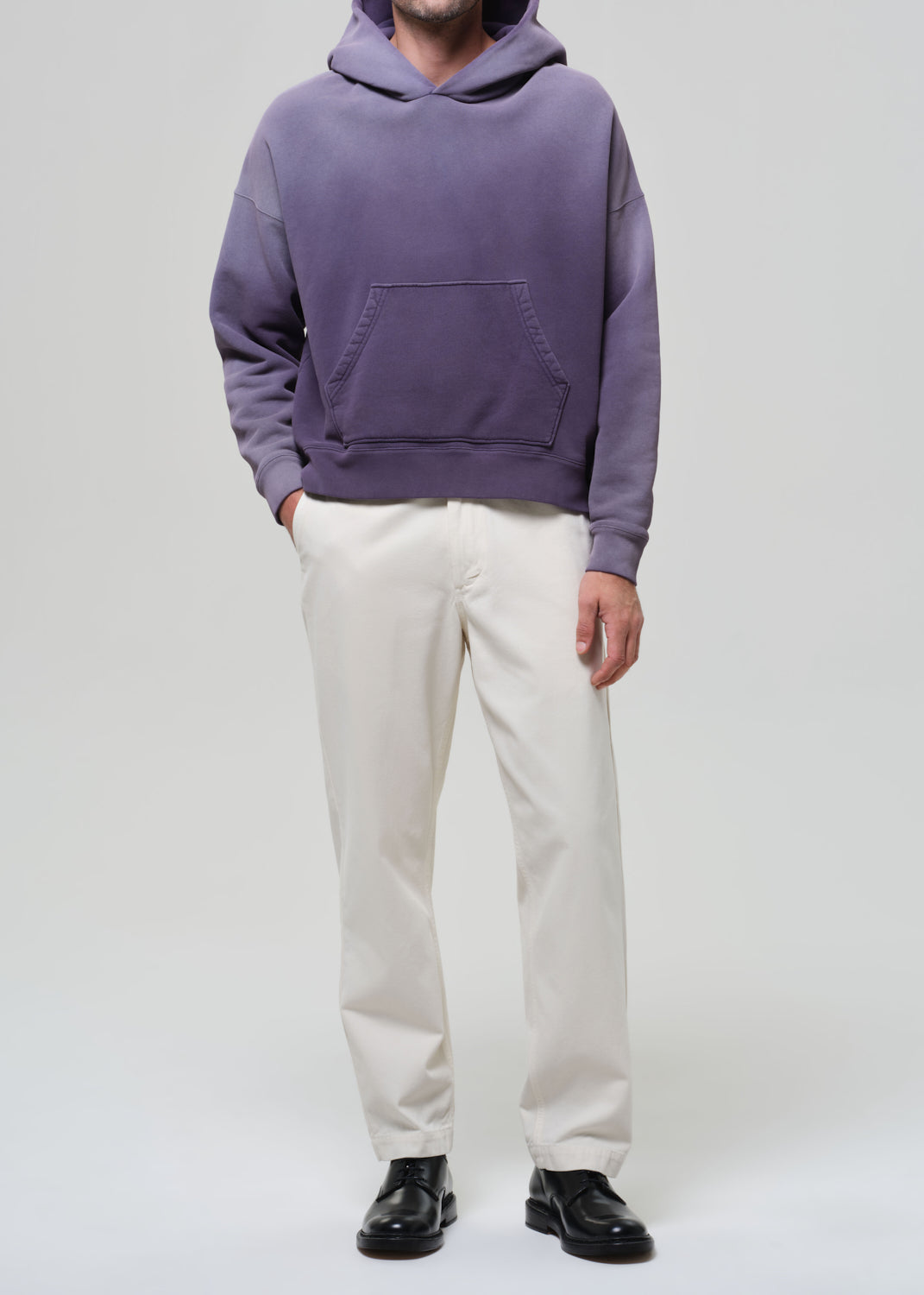 Person wearing a purple hoodie and white pants on a plain background