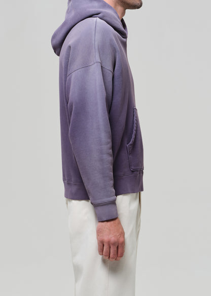 Person wearing a purple hoodie and white pants on a plain background