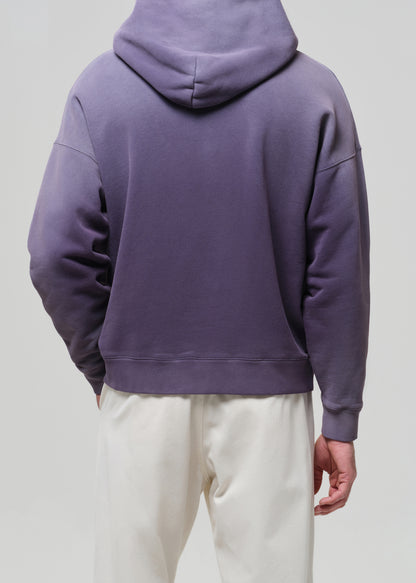 Person wearing a purple hoodie and white pants on a plain background