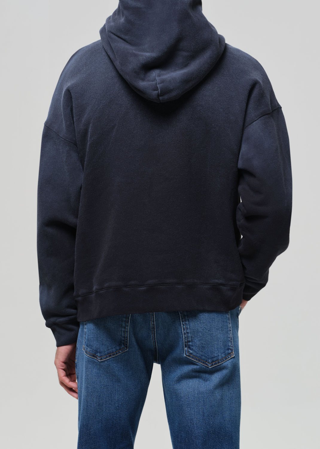 Person wearing a navy hoodie and blue jeans on a plain background