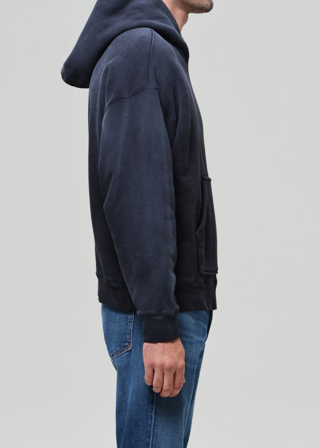 Person wearing a dark blue hoodie and jeans on a light gray background