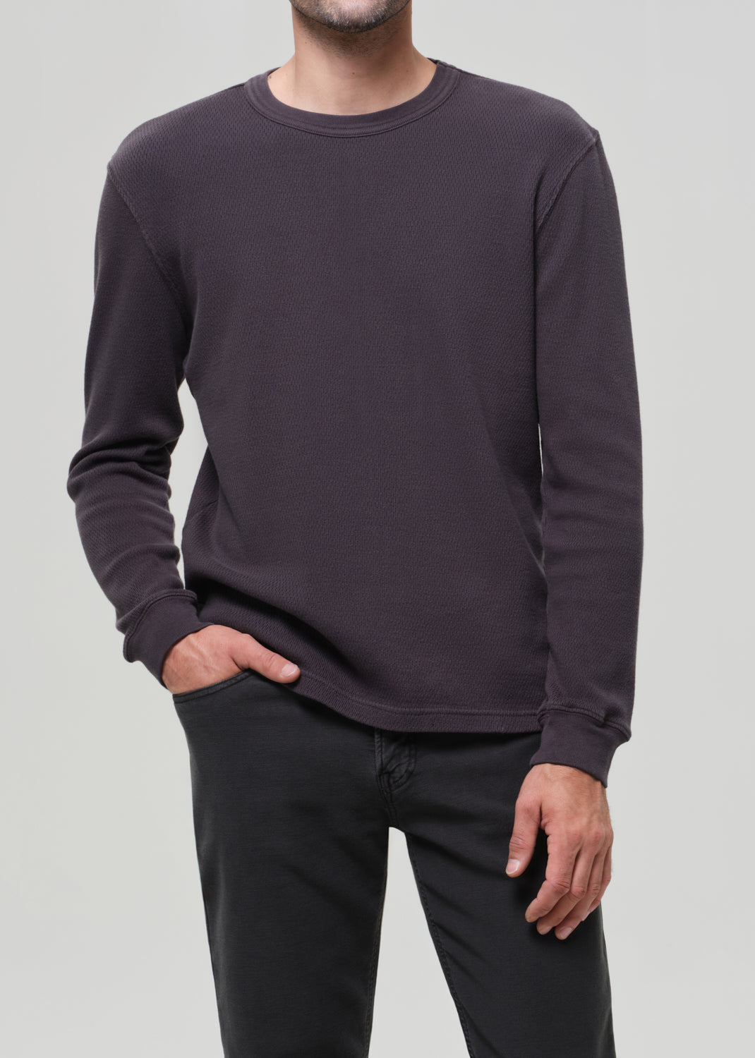 Person wearing a dark grey sweatshirt and black pants on a light gray background