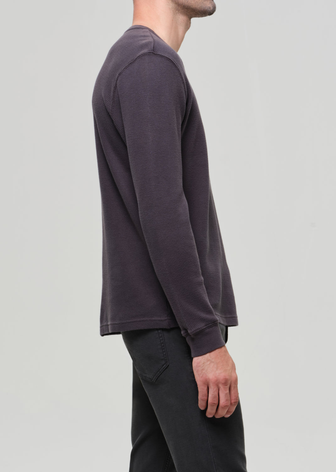 Person wearing a dark grey sweatshirt and black pants on a light gray background