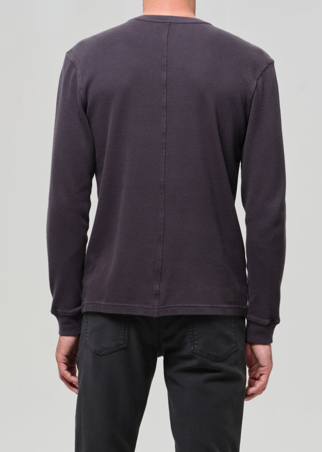 Person wearing a dark grey sweatshirt and black pants on a light gray background