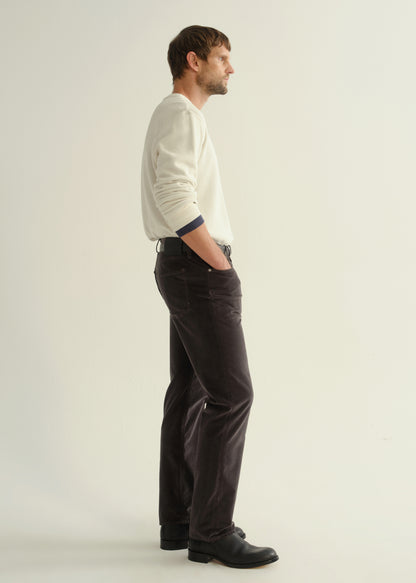 Person wearing a cream long sleeve crewneck sweater, dark brown pants, and black boots, side full body view on a light grey background.