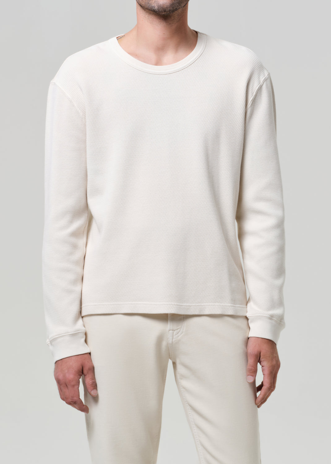 Person wearing a plain white long-sleeve shirt and pants on a light gray background