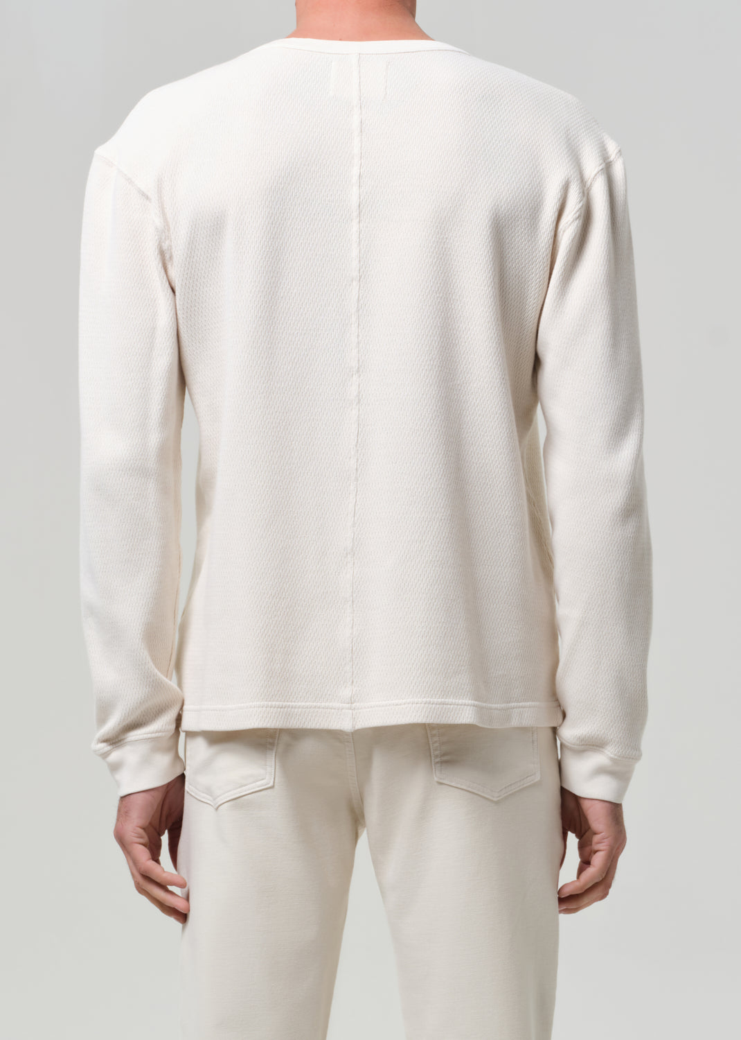 Person wearing a plain white long-sleeve shirt and pants on a light gray background