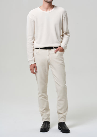 Person wearing a white sweater and cream pants with black shoes on a plain background