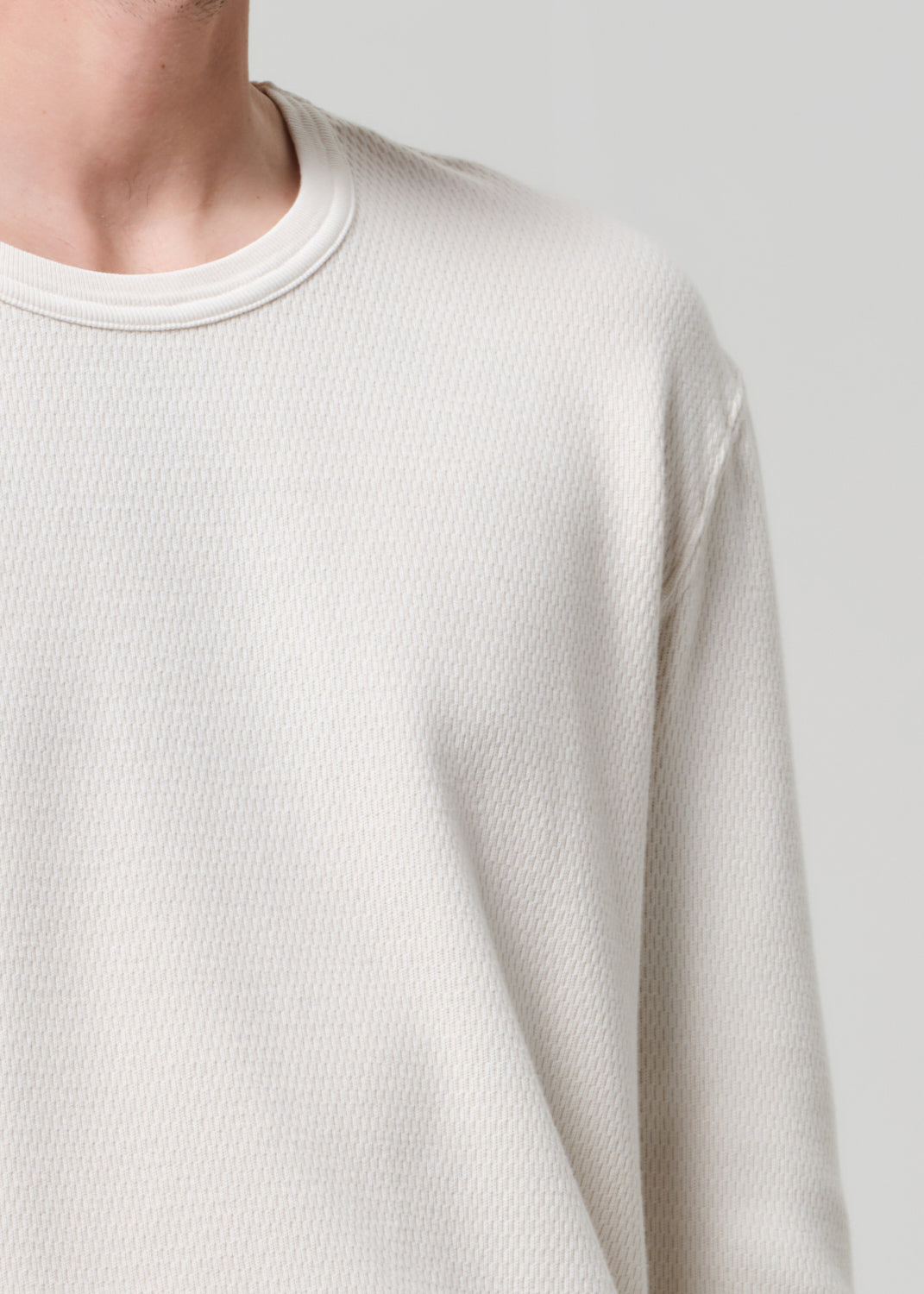 Close-up of a person wearing a textured beige sweater against a plain background