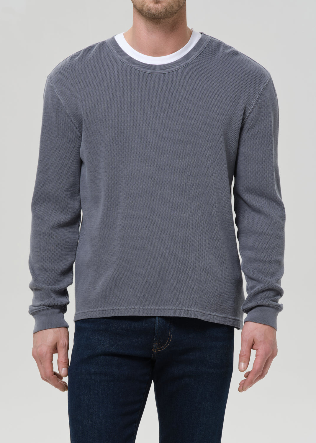 Person wearing a grey sweatshirt and dark jeans on a grey background