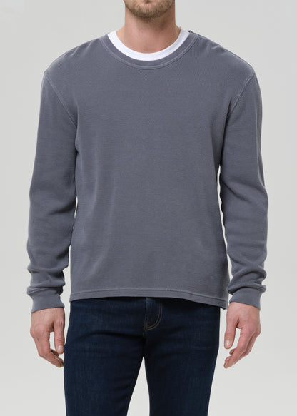 Person wearing a grey sweatshirt and dark jeans on a grey background