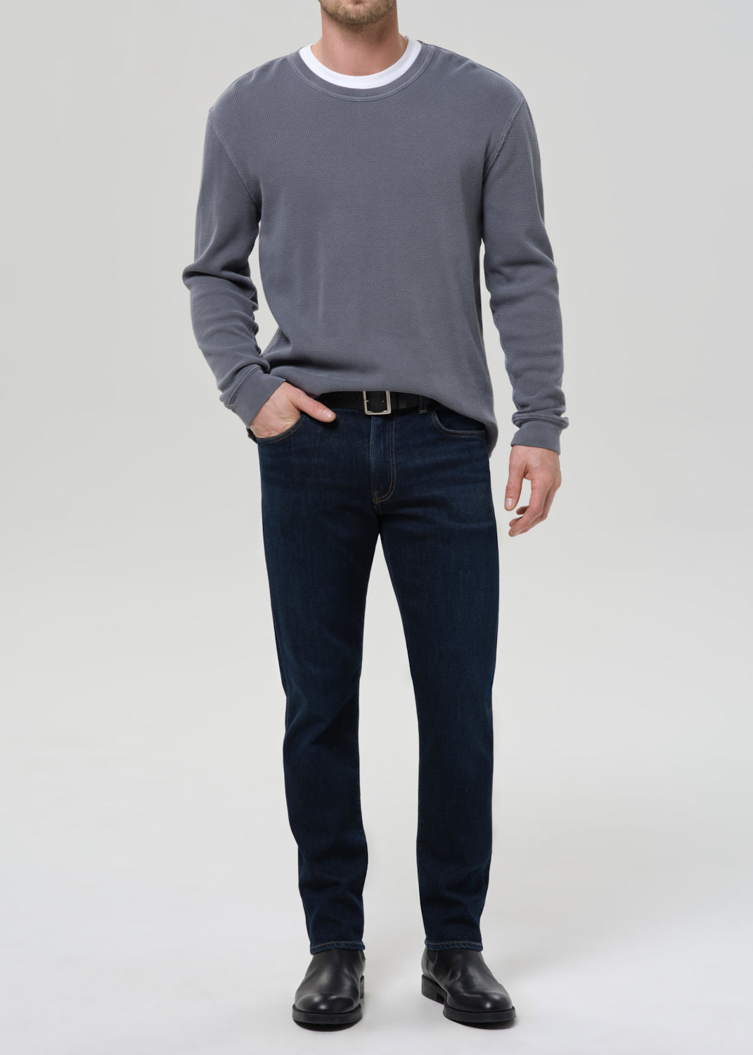 Person wearing a grey sweater and dark jeans on a grey background