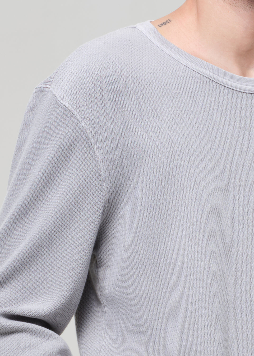 Close-up of a person wearing a light gray long-sleeve shirt against a neutral background