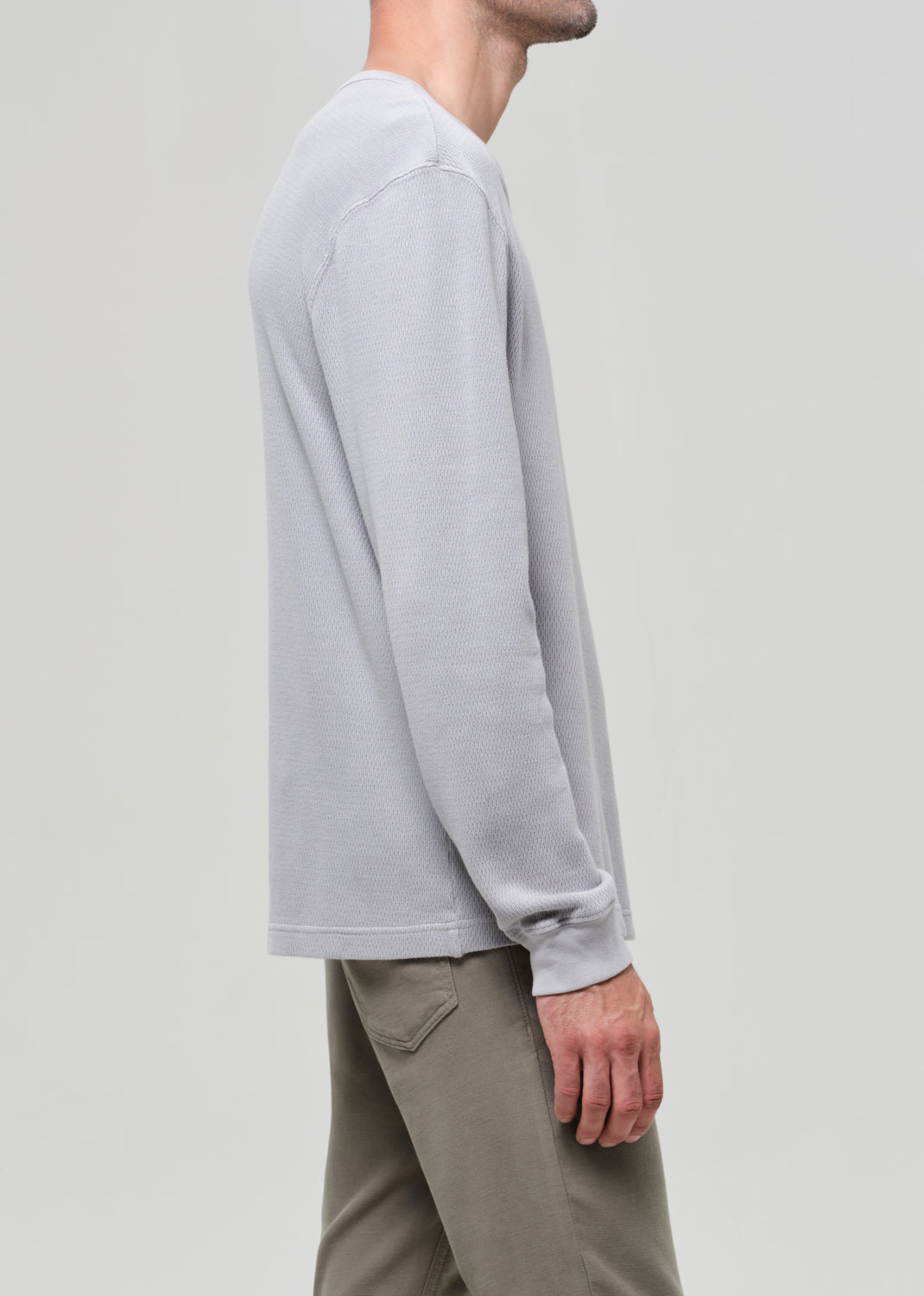 Person wearing a light gray long-sleeve shirt and beige pants on a plain background