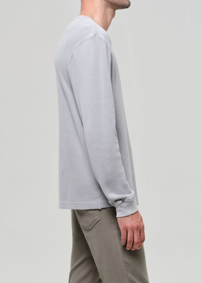 Person wearing a light gray long-sleeve shirt and beige pants on a plain background