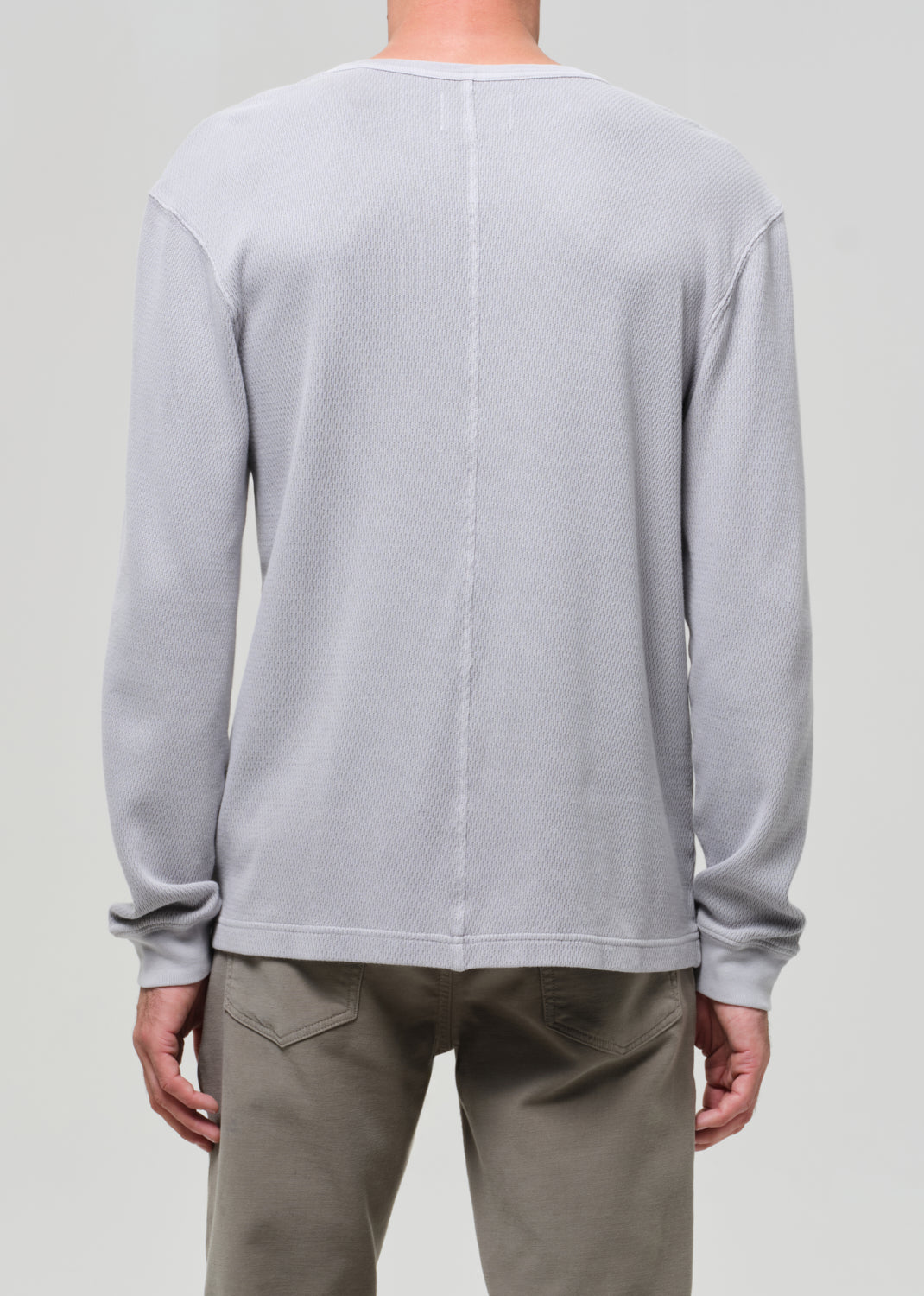 Person wearing a light gray long-sleeve shirt and beige pants on a plain background