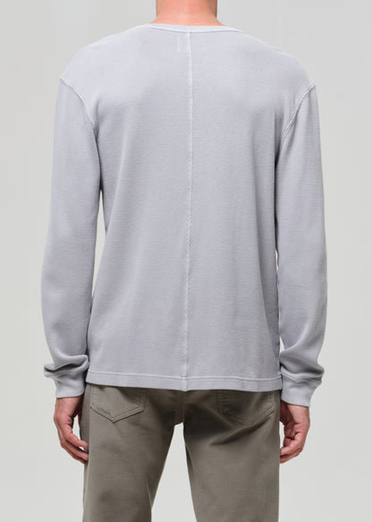 Person wearing a light gray long-sleeve shirt and beige pants on a plain background