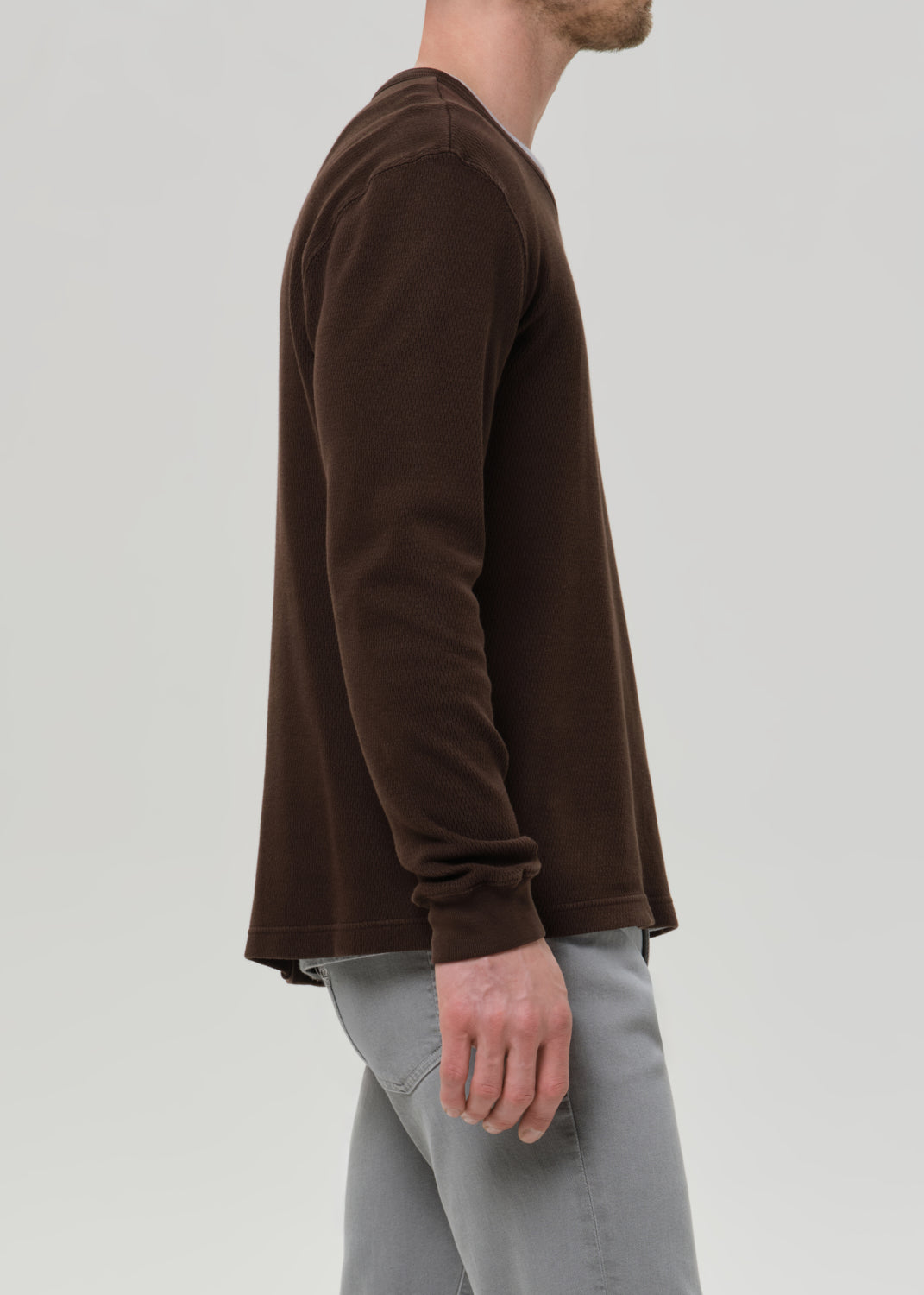 Person wearing a brown long-sleeve shirt and grey pants on a grey background