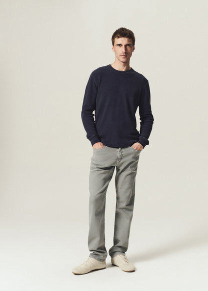 Man wearing a vintage navy waffle crewneck top with grey straight leg jeans on a grey background.