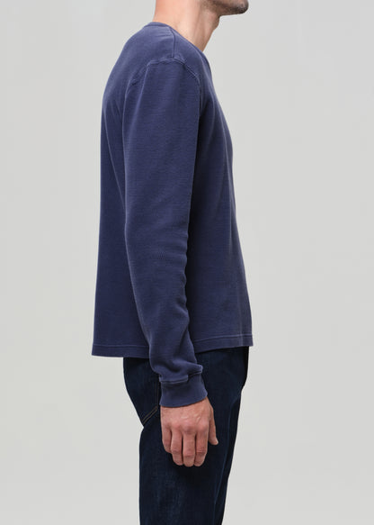 Person wearing a blue long-sleeve shirt against a gray background