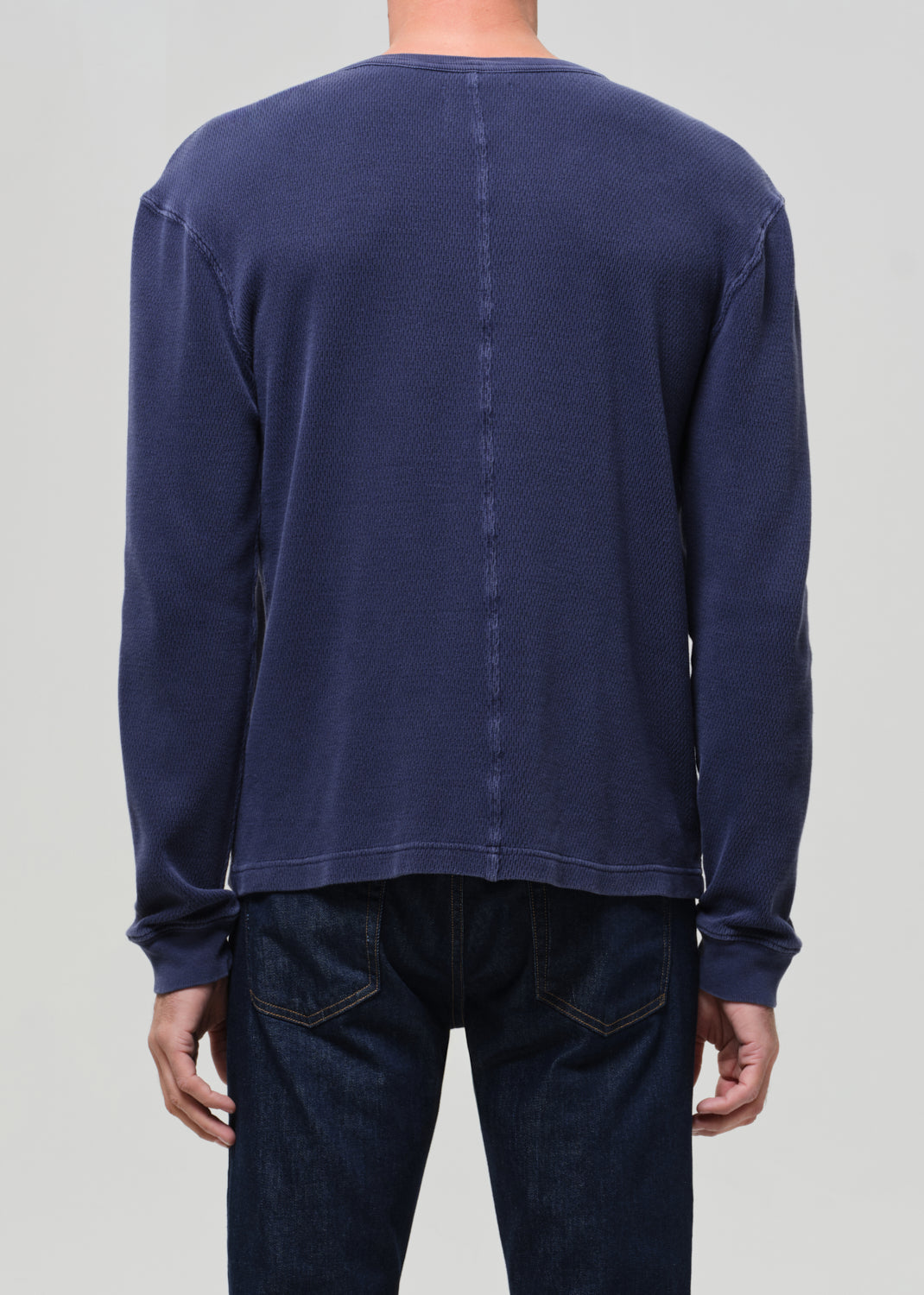 Person wearing a navy long-sleeve shirt and dark jeans on a light gray background