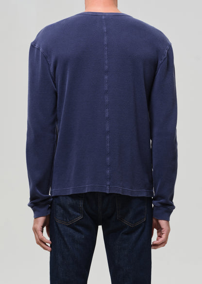 Person wearing a navy long-sleeve shirt and dark jeans on a light gray background