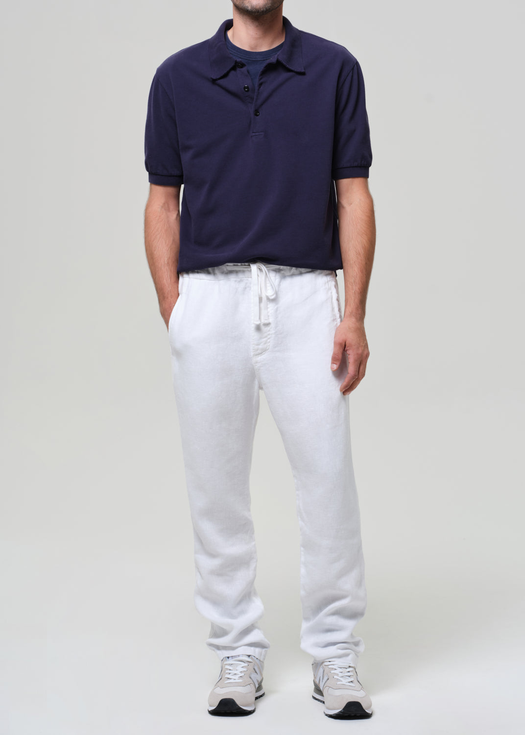 Man wearing a navy polo shirt and white pants against a plain background