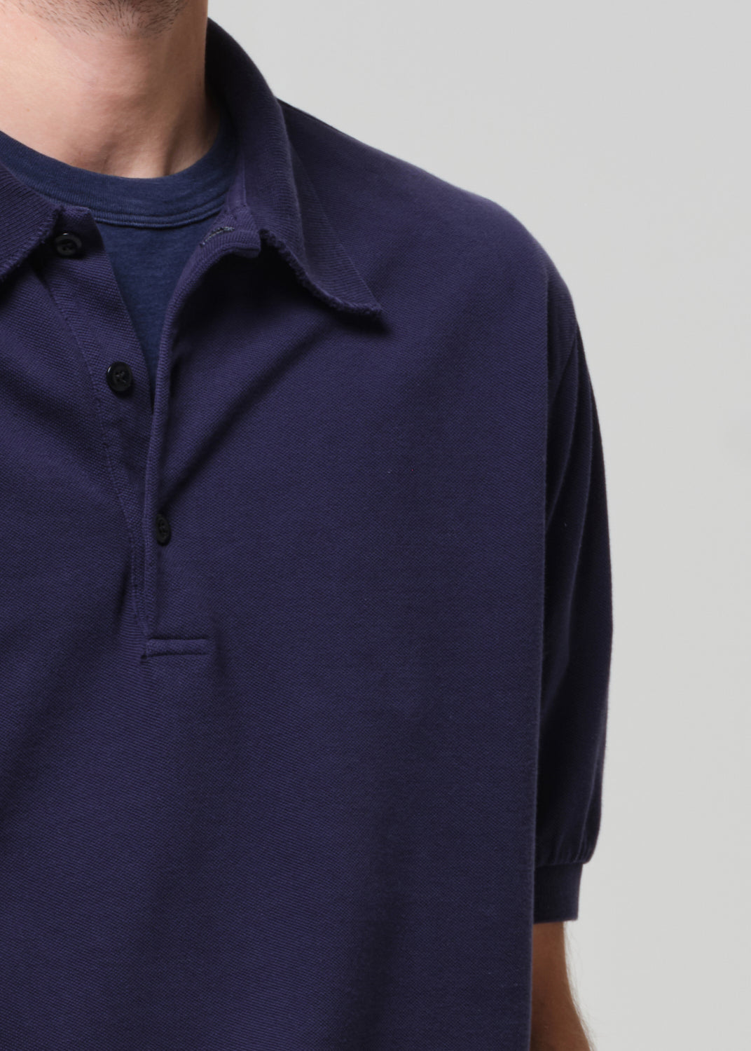 Man wearing a navy polo shirt and white pants against a plain background