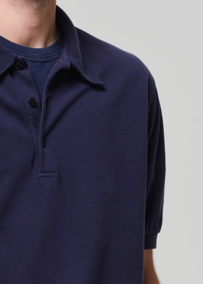 Man wearing a navy polo shirt and white pants against a plain background