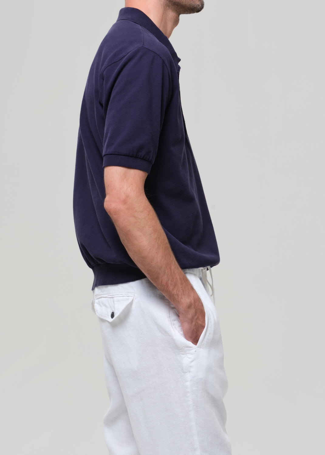 Man wearing a navy polo shirt and white pants against a plain background