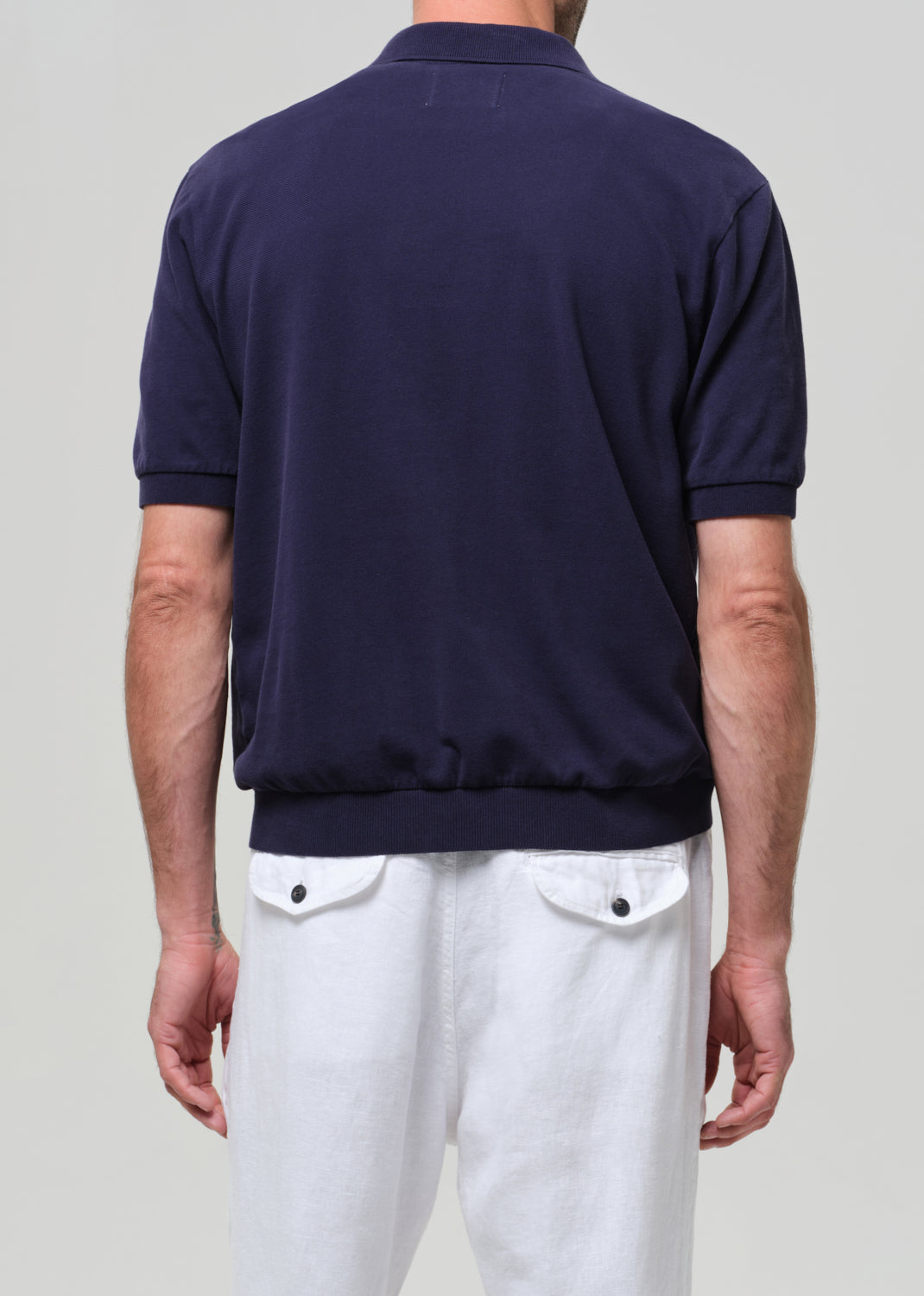 Man wearing a navy polo shirt and white pants against a plain background