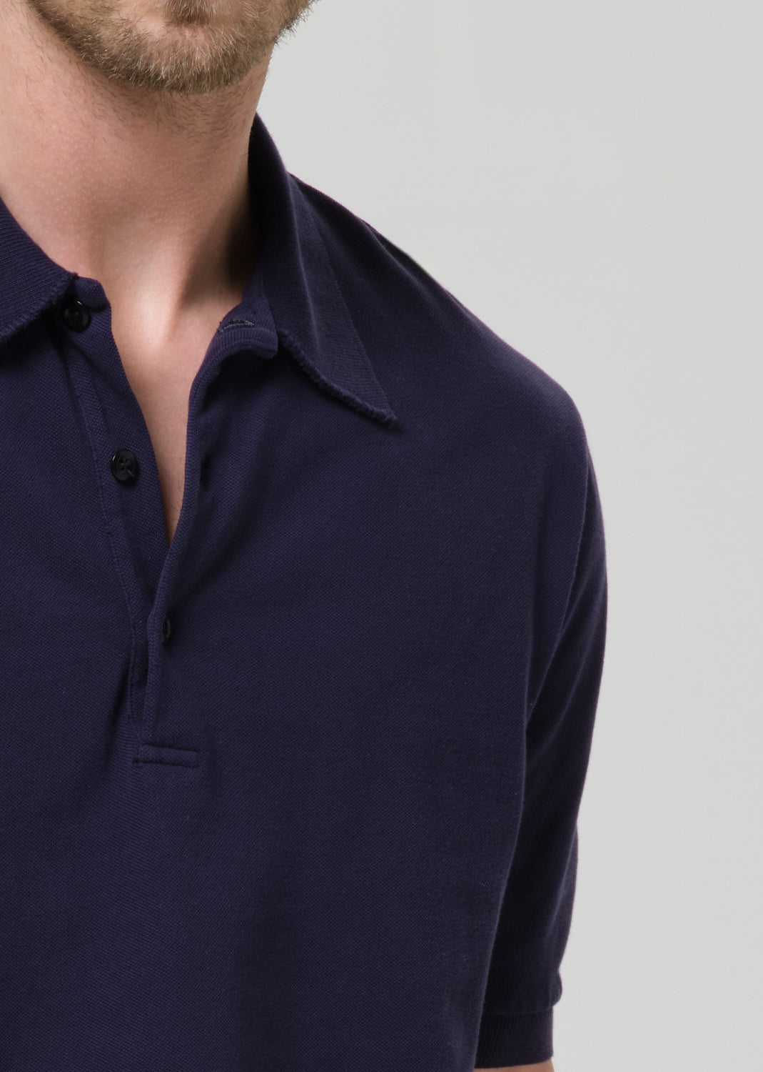 Close-up of a man wearing a dark navy blue short-sleeve polo shirt against a grey background.
