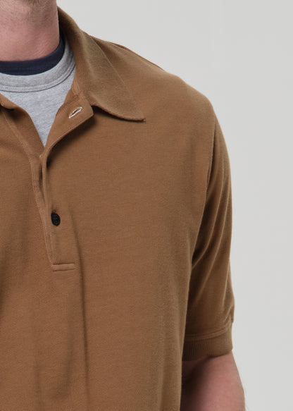 Close-up of a man wearing a brown short-sleeve polo shirt over a gray t-shirt, against a grey background.