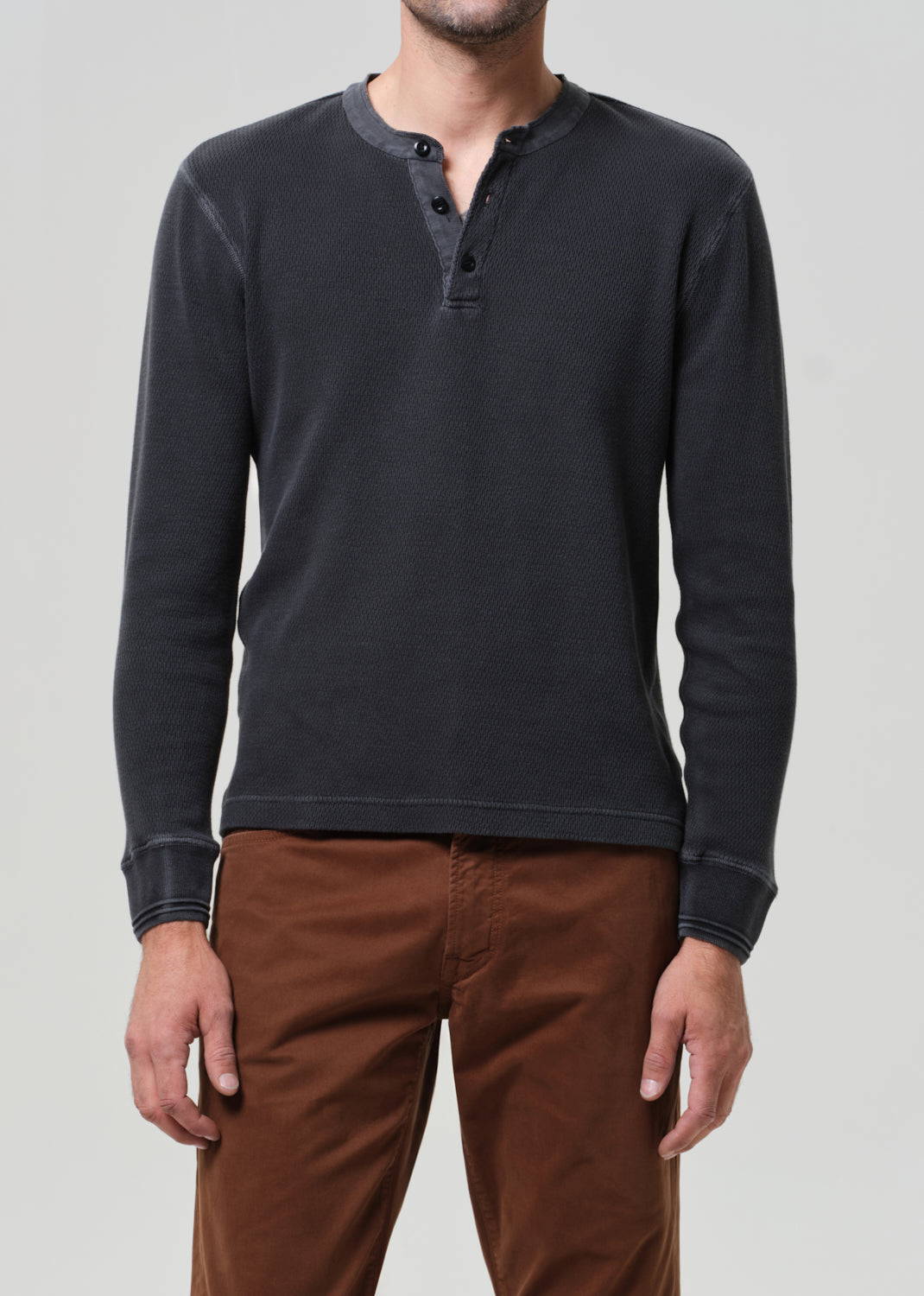 Person wearing a dark gray long-sleeve henley shirt and brown pants on a light gray background