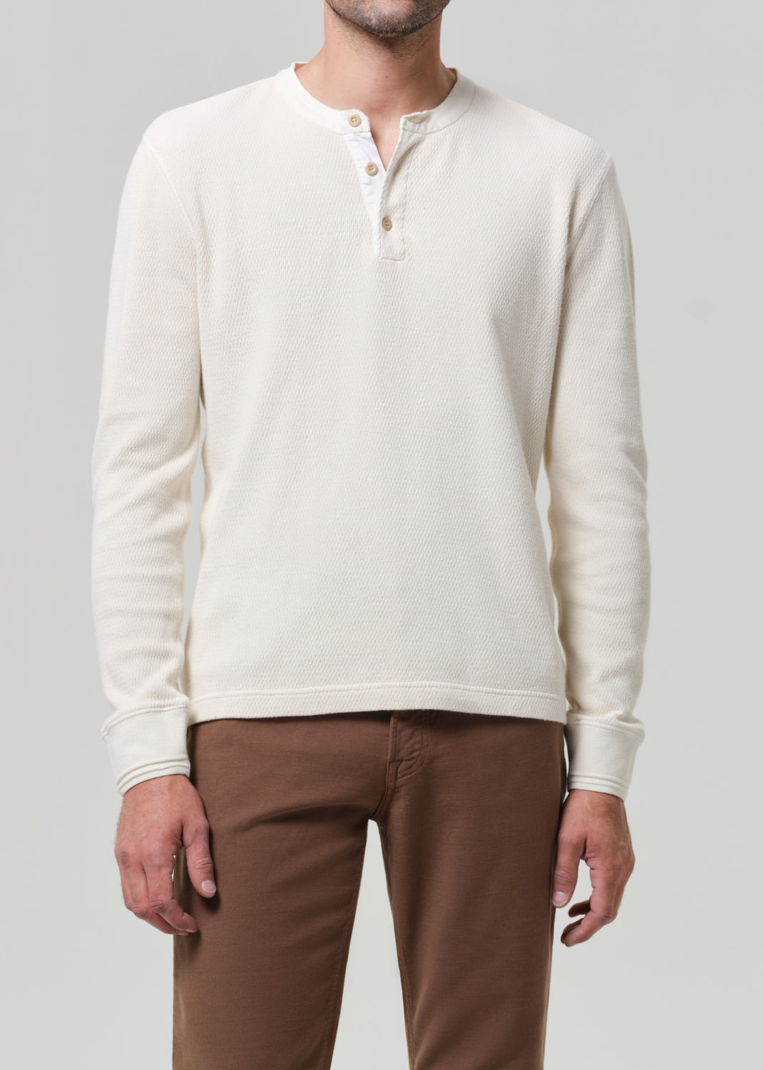 Person wearing a cream-colored sweater and brown pants on a gray background