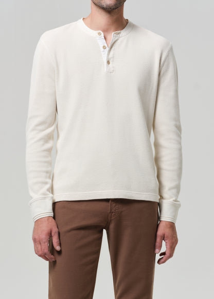 Person wearing a cream-colored sweater and brown pants on a gray background