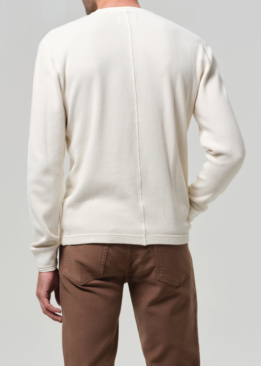 Person wearing a cream sweater and brown pants on a plain background