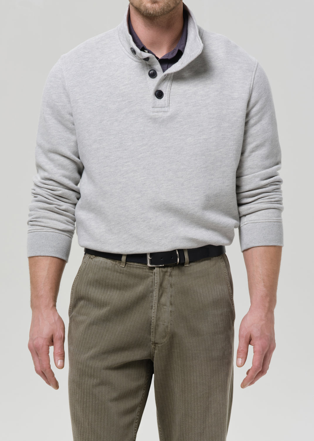 Man wearing a grey sweater and beige pants against a grey background