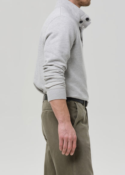 Person wearing a grey hoodie and green pants on a grey background