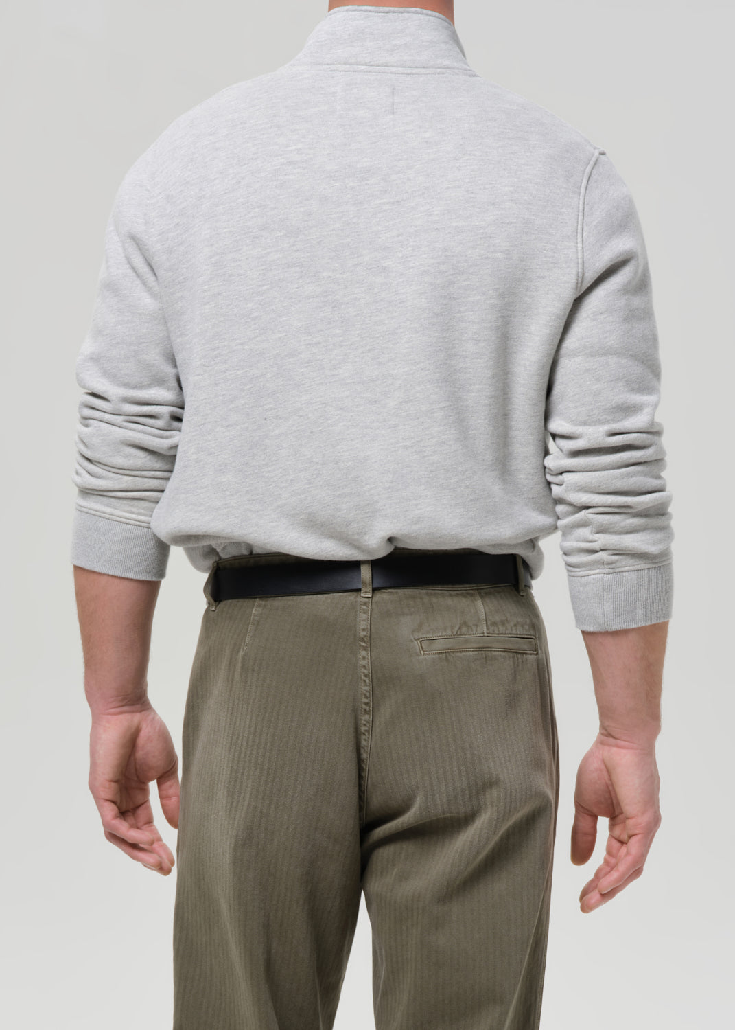 Person wearing a grey sweater and beige pants on a grey background