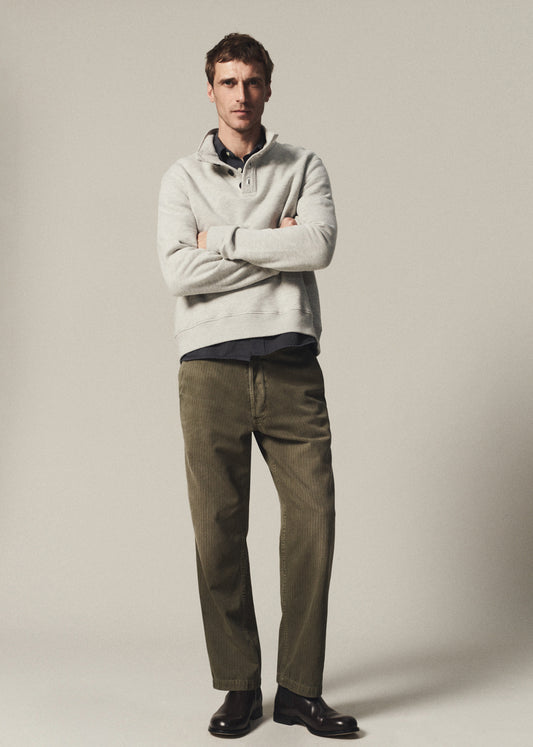 Man wearing a heather grey half-button pullover layered over a navy button-up shirt with olive pants on a grey background.