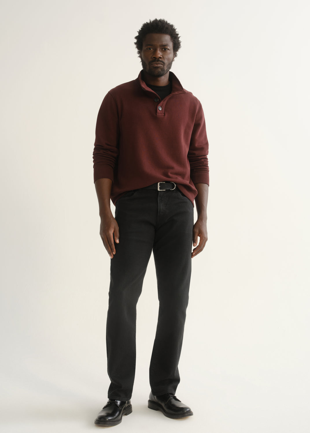 Person wearing burgundy half-button pullover with black pants and black shoes, side view