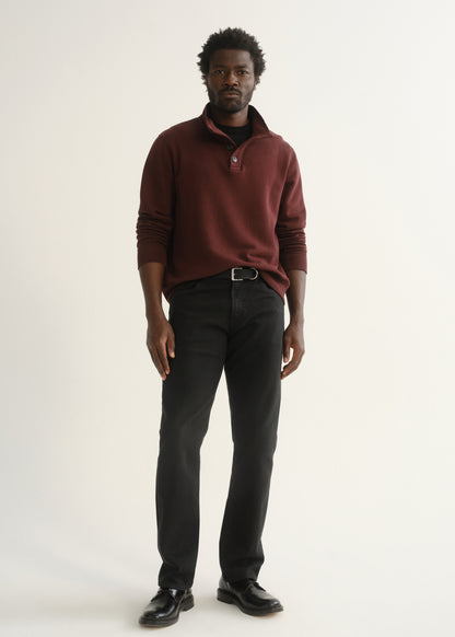 Person wearing burgundy half-button pullover with black pants and black shoes, side view