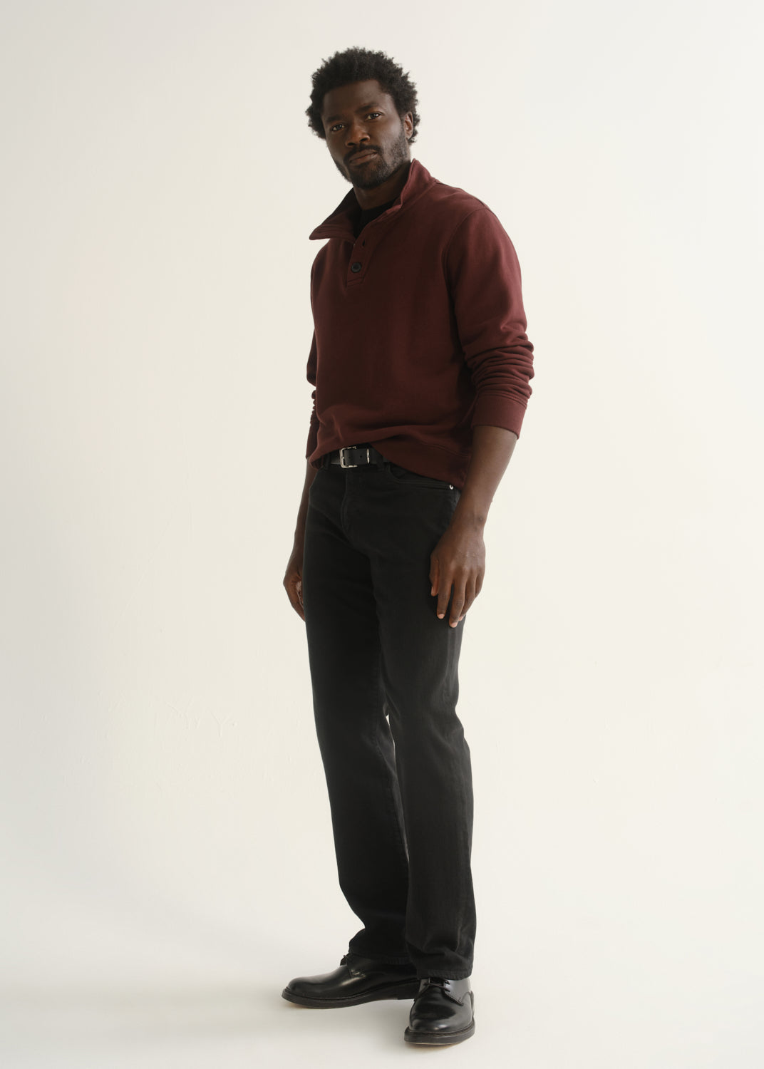 Person wearing burgundy half-button pullover with black pants and black shoes, back view