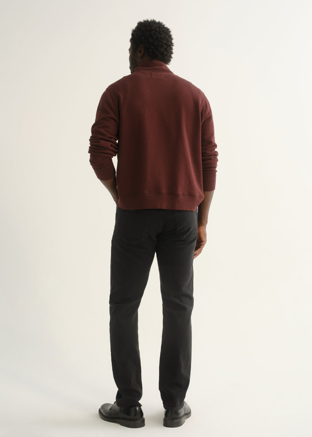 Person wearing burgundy half-button pullover with black pants and black shoes, front view